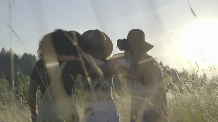 Three woman put arms around each other and sway in field
