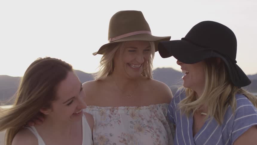 A group of three friends stand out in the dry barren soil cracking landscape of a desert with a sunset and mountain range behind them