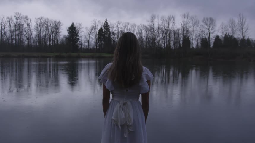 Woman wearing a white dress looks out at a lake