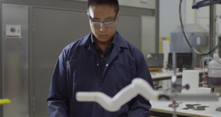 A man in a blue lab coat approaches a table in a laboratory