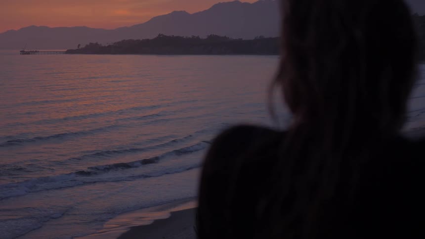A woman watches the sun set over the ocean