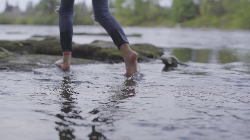 A woman walks out of the water and onto a rock