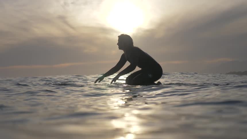 A person kneeling on a surfboard in the water