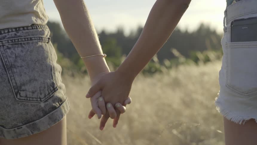 Two women hold hands in the tall grass