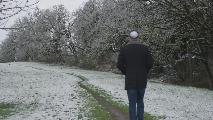A man wearing a yamaka walks down a green path that has no snow