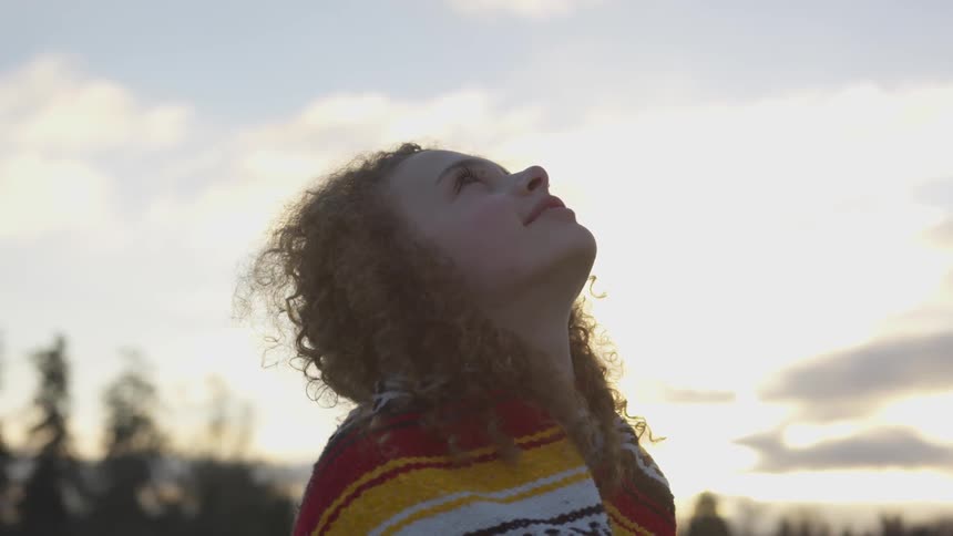 A curly haired girl wrapped in a blanket looks up at the sky