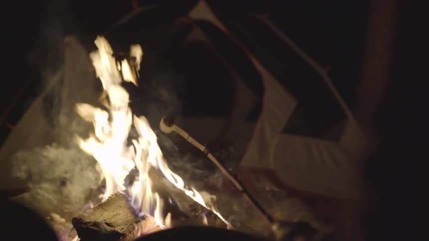 Person sits by tent roasting a marshmallow