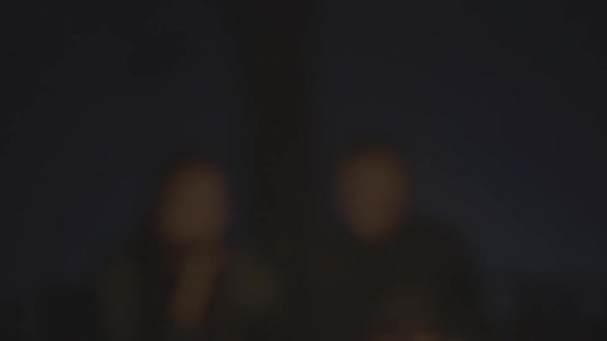 Blurry shot of a couple near a fire on a dark night with embers flying up in front of their dimly lit faces