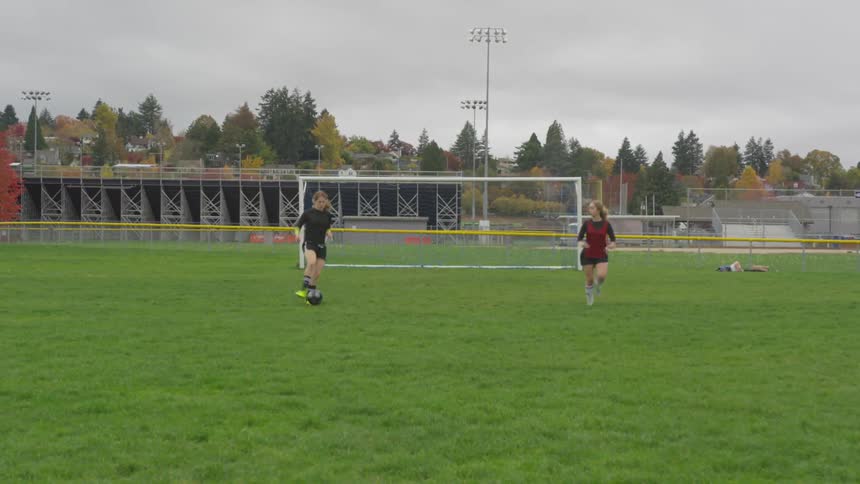 Two girls practice passing a soccer ball on a field