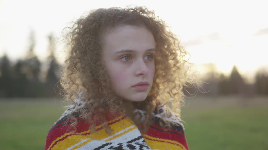 Girl standing in a field wrapped in a vivid blanket