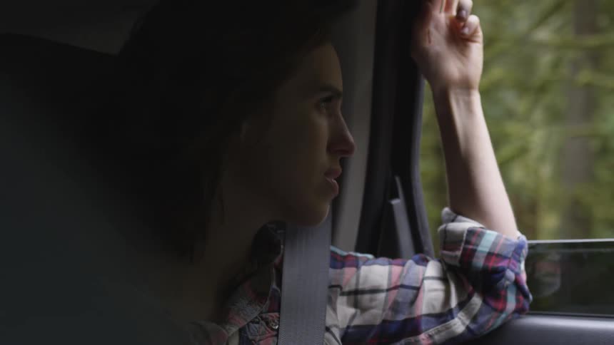 A woman riding in a vehicle looking out of the window at a forest