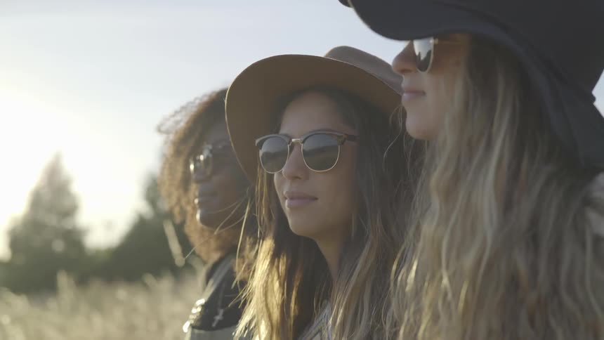 3 women wearing sunglasses stare into the distance at noon