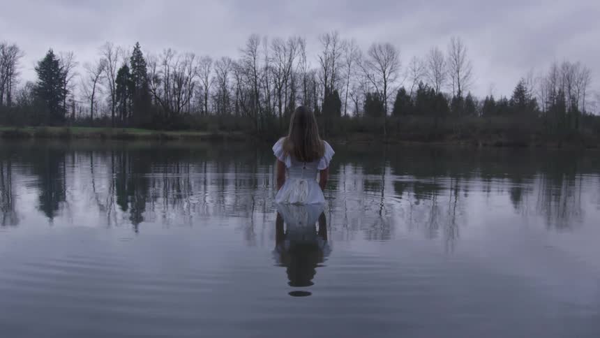A woman is standing waist deep in the lake