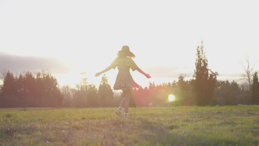 A woman twirls in a large empty field under the sun