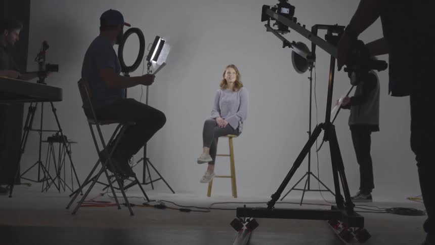 A model sits on a stool in a photo studio