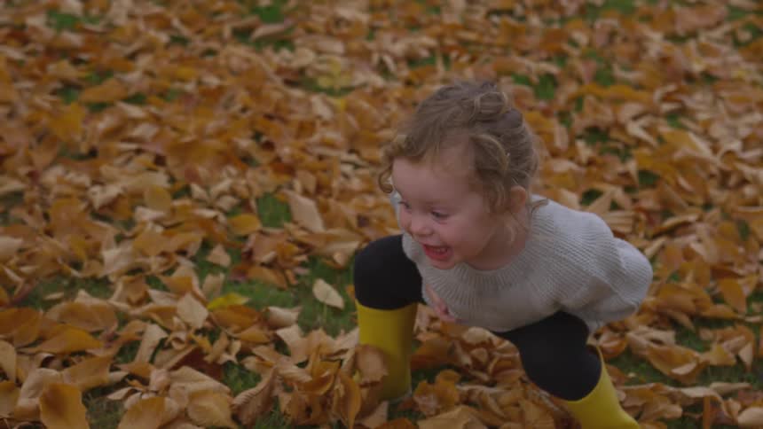 A child squatting and laughing in a leafy yard