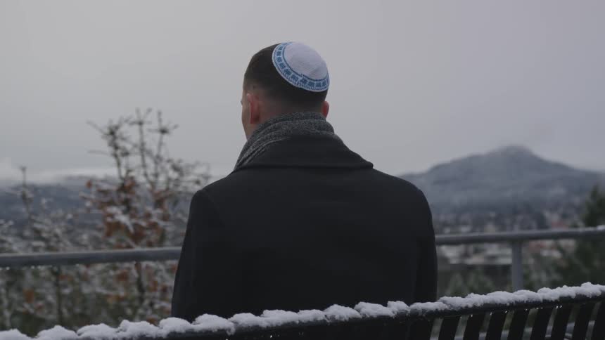 Man in yarmulke sits on bench in the snow