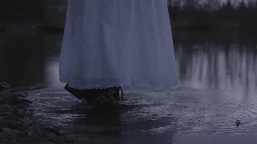 A woman wearing a white dress and work boots walks into water