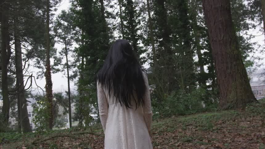 Girl in white dress stands in the middle of the woods on a cloudy day she looks creepy and kinda like a ghost