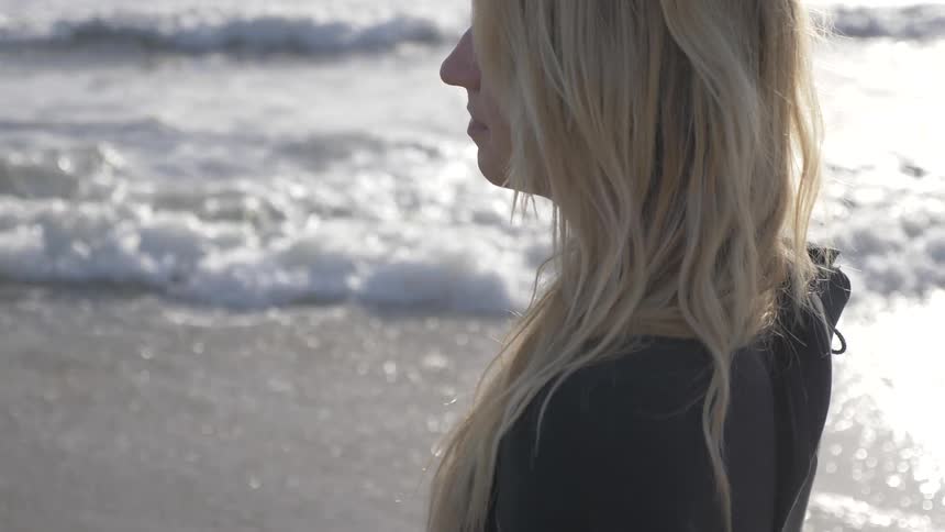 A woman stands on the beach as waves come to shore
