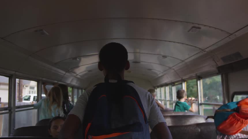 A boy with a backpack walks down the aisle of a bus