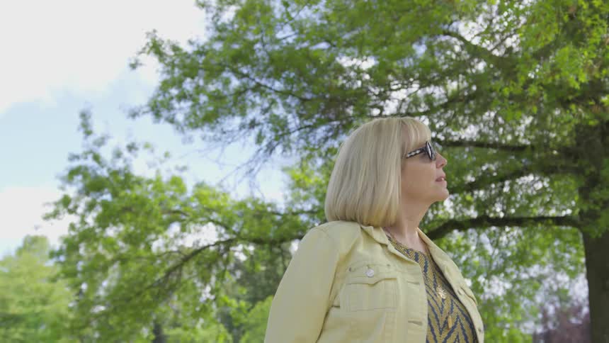 Woman watches sky as she walks near trees on a sunny day