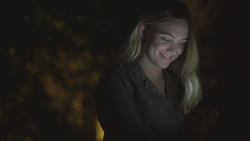 A woman smiles as she sits under trees in the dark