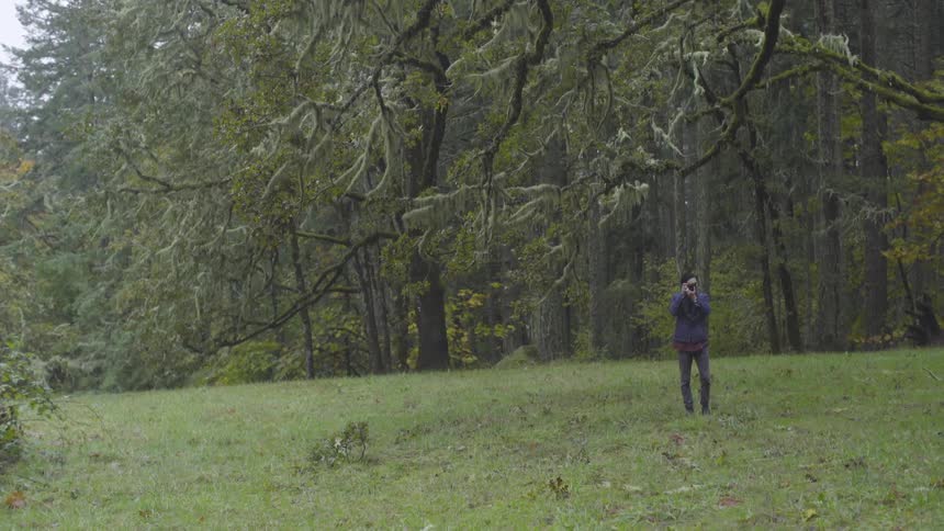 Man stands in a field taking pictures of trees