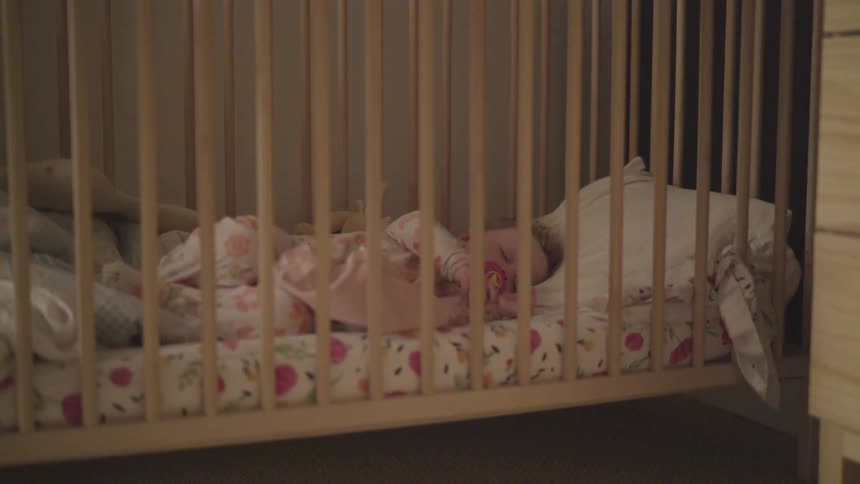 A baby girl sleeps in a crib while sucking on a pacifier