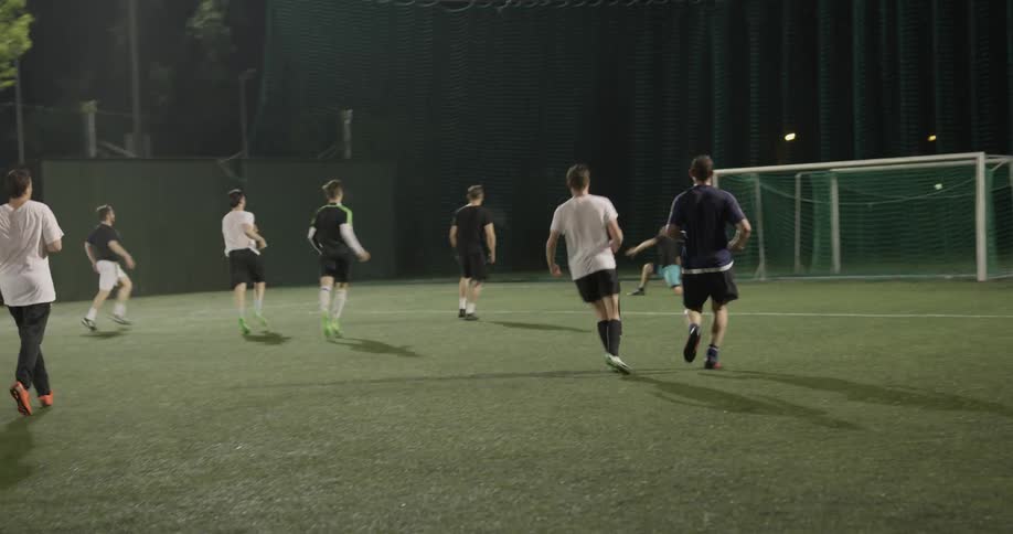 Group of men of different ages playing soccer on a field at night