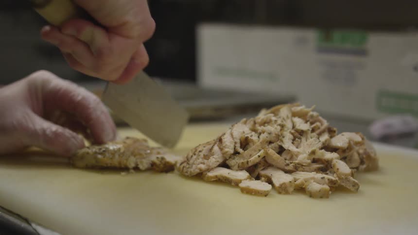 A chef cuts chicken on a cutting board