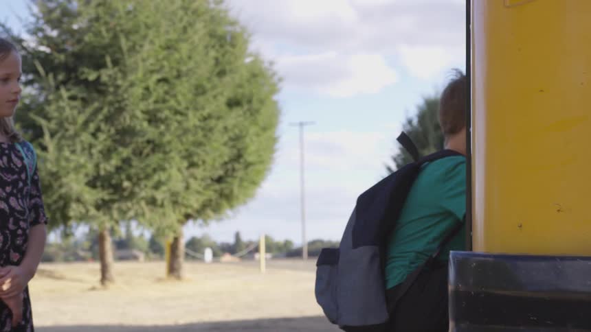 Boy gets on school bus as girl waits