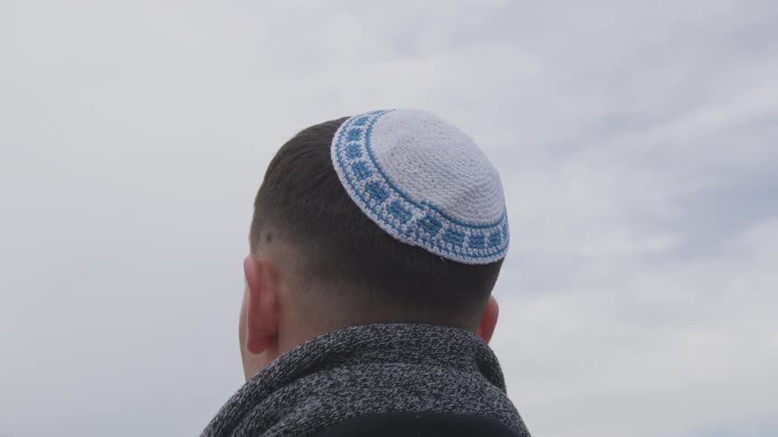 A blue and white yarmulke on a man's head on a cloudy day