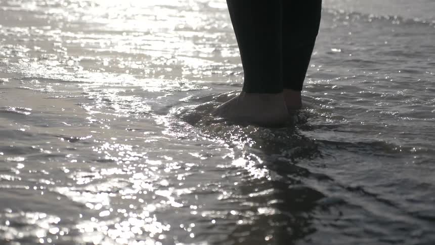 Person standing on the beach with waves crashing into their feet