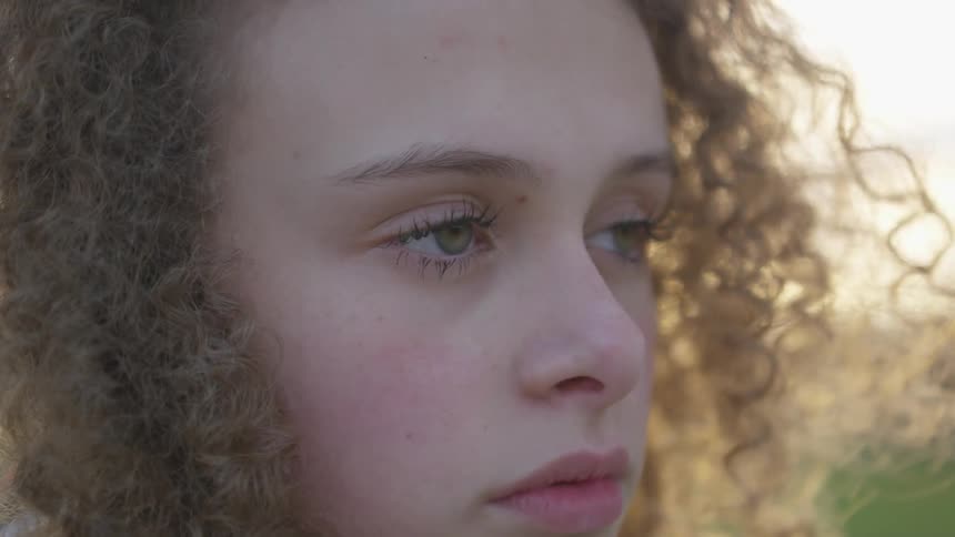 Young girl with green eyes and curly hair looks off camera and blinks