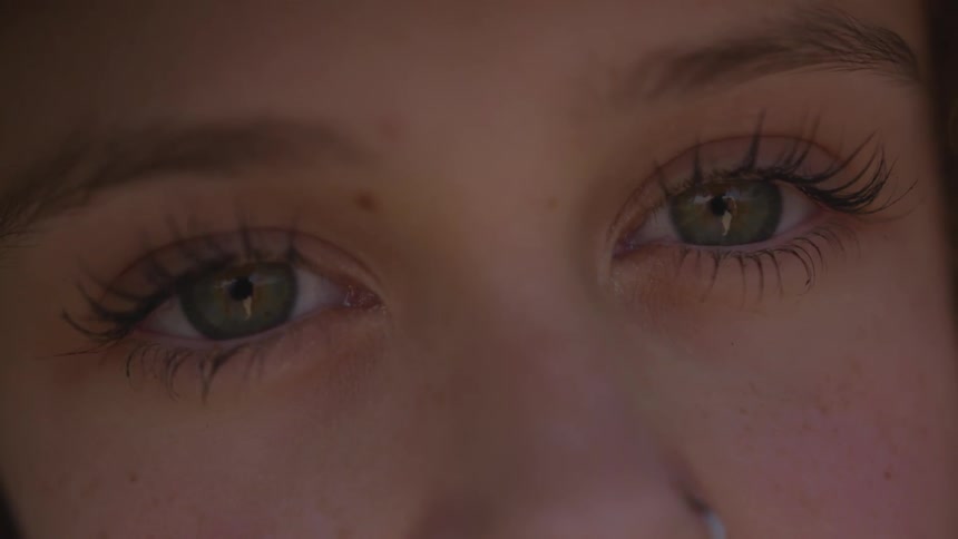 A woman wearing mascara blinks her eyes outside