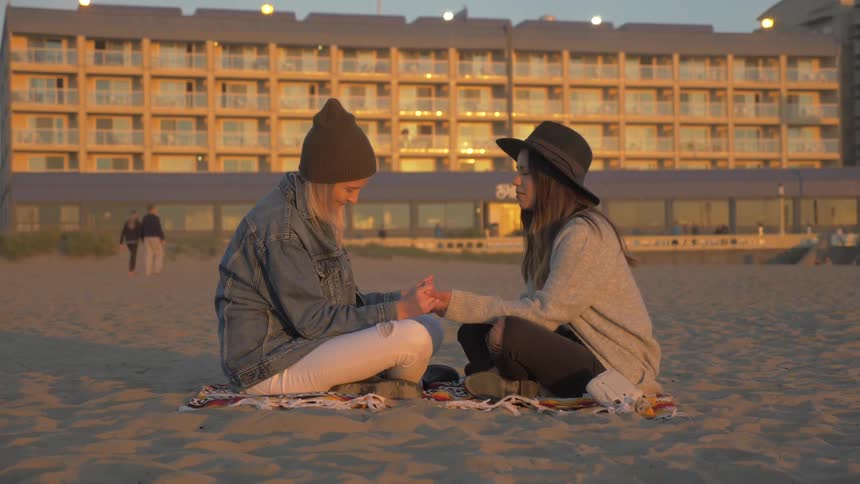 Two females sit on the beach and hold hands while praying