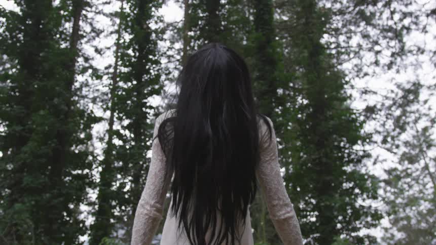 A woman walking in a forest while wearing a white dress