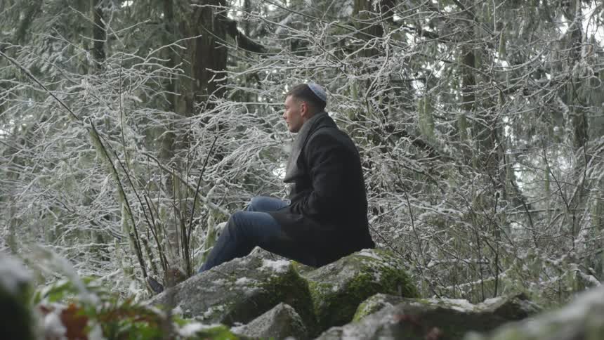 A man in a coat sits in a snowy forest