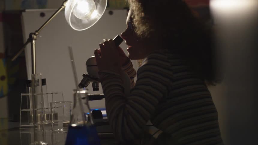 Young girl looks into microscope at desk