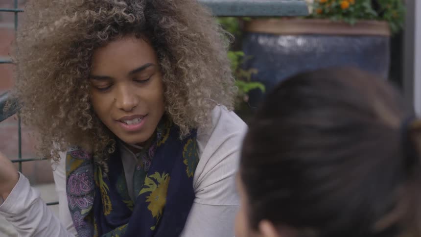 Young woman with curly hair talks to friend outdoors
