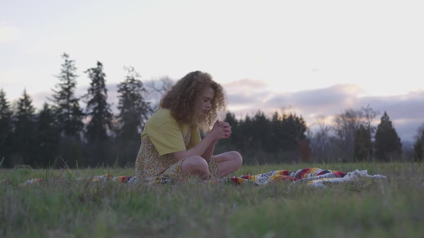 A woman sitting on a blanket with her hands clasped together