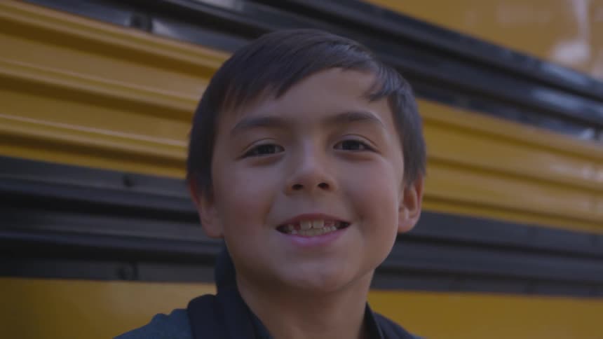 A boy smiling in front of a school bus