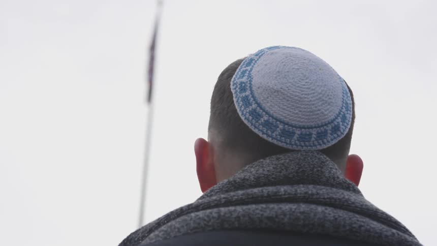 A man wearing a yamaka looks up at a flag at the top of a flag pole