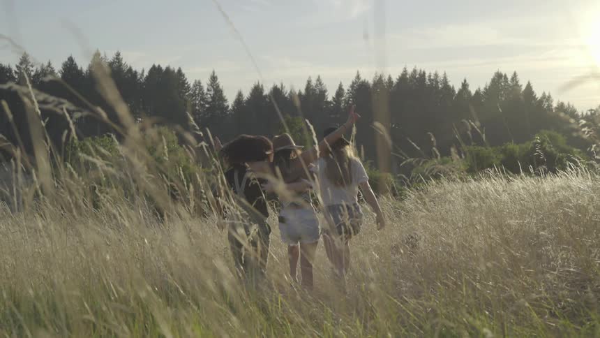 Three young women walk through field and put arms around each other