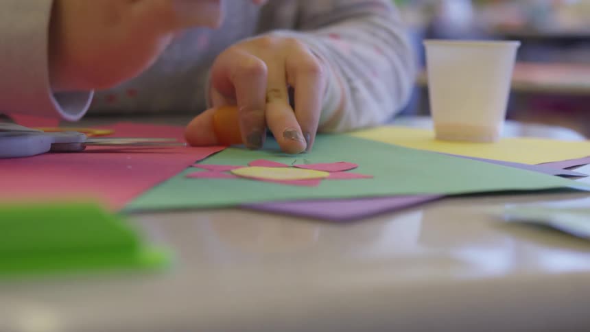 A little girl paints her nails as her hands sit on construction paper