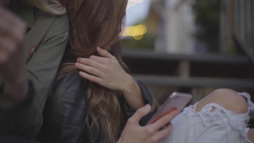 Two young women sit on steps looking at cell phones