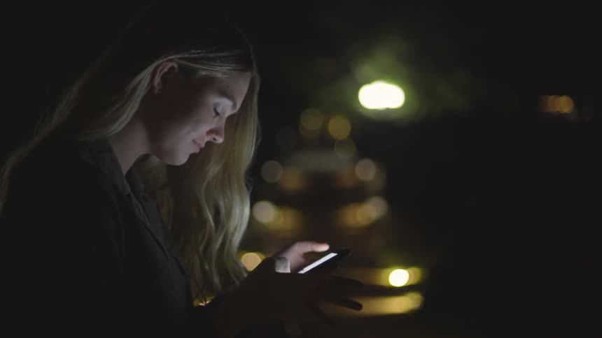 Woman reads her phone outside at night