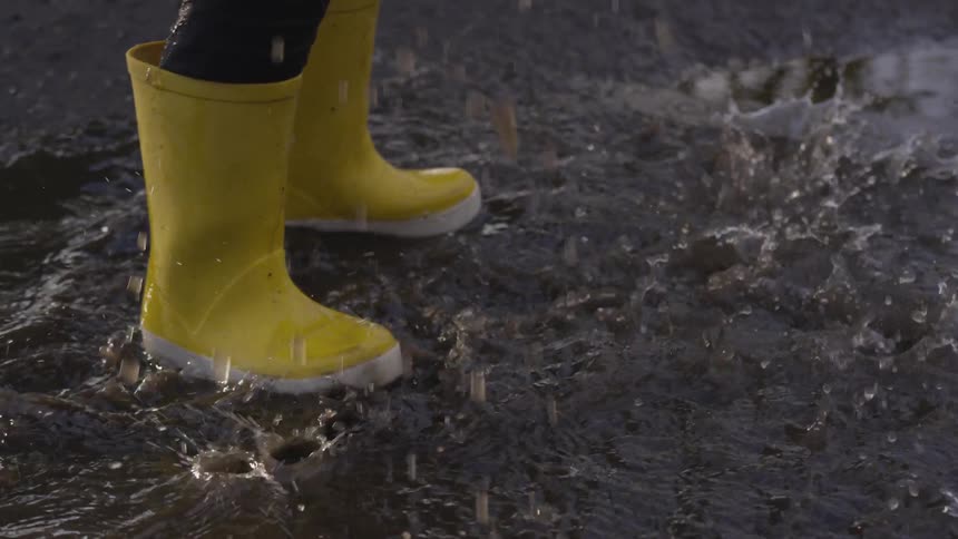 Yellow rain boots stomp a puddle