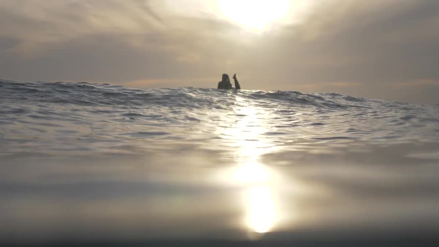 A surfer rides on their board over the crest of a gentle wave
